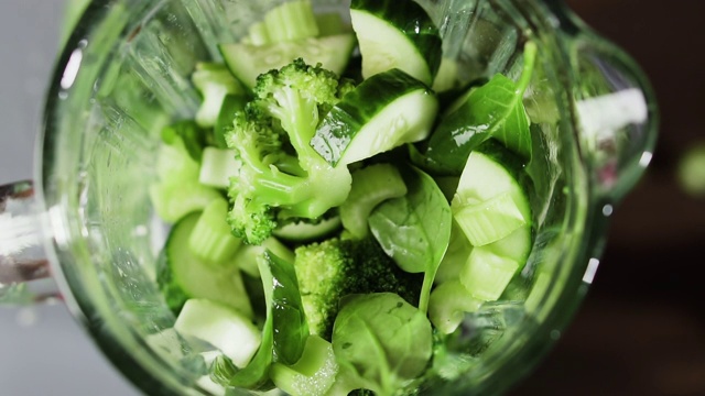 蔬菜落到搅拌机里，慢动作。绿色奶昔在搅拌机，俯视图。健康饮食的概念。视频素材