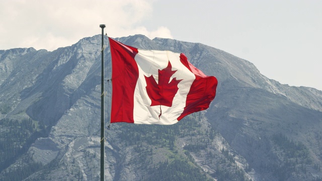 加拿大国旗在风中吹动的慢动作镜头与山在一个阳光明媚的日子的背景视频下载