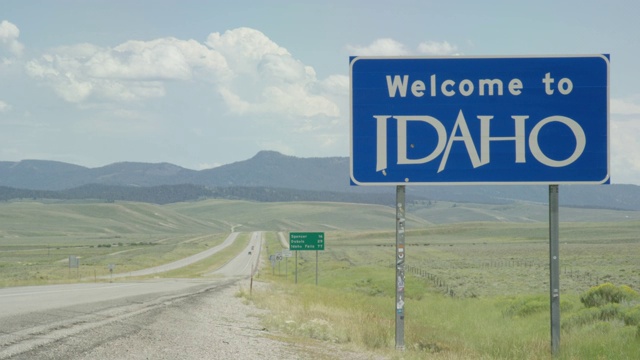 汽车和车辆驶过怀俄明州/爱达荷州边界上的“欢迎来到爱达荷”州标志，在一个阳光明媚的日子里，背景是群山视频素材