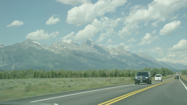 移动镜头从一辆汽车沿着高速公路行驶平行于大提顿山脉在大提顿国家公园在西怀俄明州在一个阳光明媚的日子视频素材