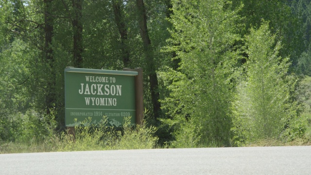 在一个阳光明媚的日子里，汽车和车辆在怀俄明州的灌木丛中经过“欢迎来到杰克逊”的标牌视频素材