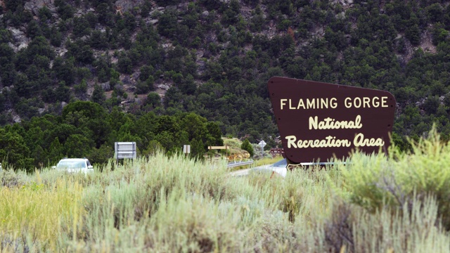 汽车和车辆驾驶的“火红峡谷国家休闲区”标志旁边的道路在犹他州山脉附近火红峡谷视频素材