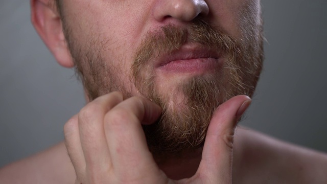 一个年轻人用手摸了摸他的大胡子和小胡子，特写。视频素材