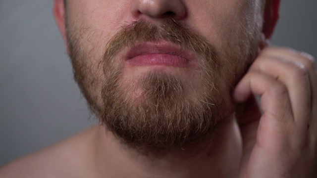 一个年轻人用手摸了摸他的大胡子和小胡子，特写。视频素材