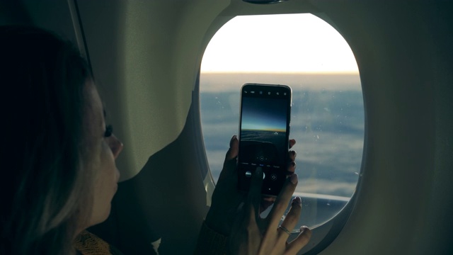 一个女人在飞机上拍照时手里拿着手机视频下载