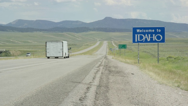 汽车和车辆驶过怀俄明州/爱达荷州边界上的“欢迎来到爱达荷”州标志，在一个阳光明媚的日子里，背景是群山视频素材