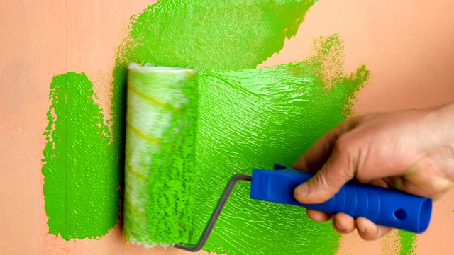 人用手用漆辊把粉红色的墙壁涂成亮绿色。视频素材