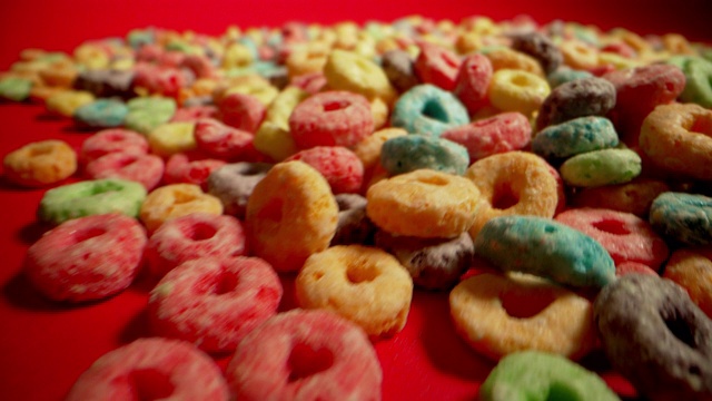 微距特写广角移动拍摄的糖彩色水果环美国早餐麦片摊开在一个红色的背景视频下载