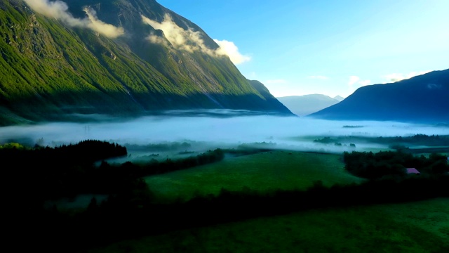 晨雾笼罩着阳光下群山间的山谷。挪威的雾和美丽的自然航拍镜头。视频下载