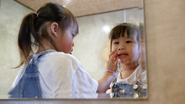 可爱的小女孩在房间里对着镜子化妆和涂口红。视频素材