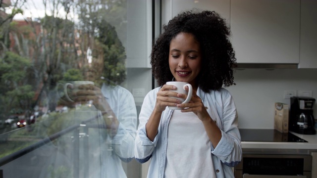 年轻宁静的黑人妇女在家看着窗外，享受着咖啡，然后对着镜头微笑视频素材