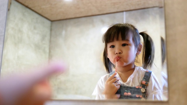可爱的小女孩在房间里对着镜子化妆和涂口红。视频素材