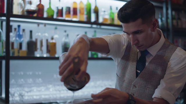 男调酒师将酒精从鸡尾酒调酒器倒入玻璃杯，同时制作饮料视频素材