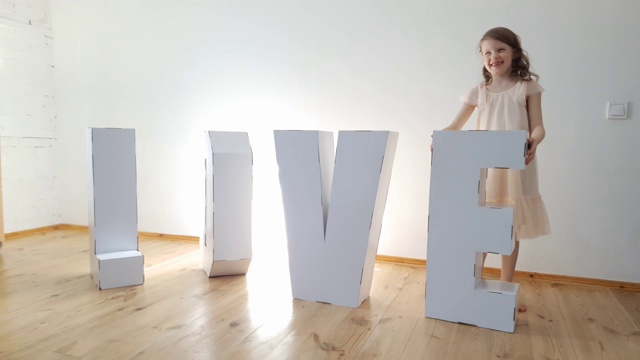 7岁的女孩玩大纸板3D站立字母从白色纸板形成单词爱在一个轻的背景。关系的概念视频素材