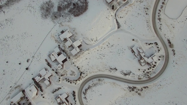 鸟瞰图的空曲线道路由积雪覆盖的房子在城镇，无人机移动在蜿蜒的高速公路在冬天-杰克逊，怀俄明州视频下载