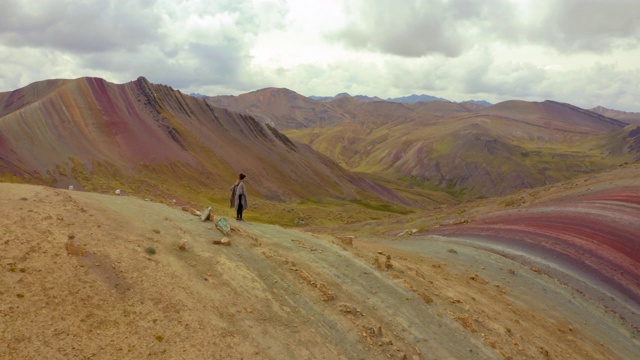 在云雾笼罩的天空下，女人在山上张开双臂奔跑的鸟瞰图，人们在美丽的风景上——彩虹山，秘鲁视频下载