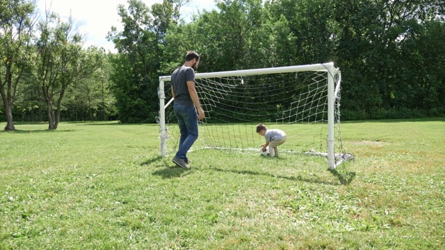 年轻的父亲和他的小儿子在足球场上踢足球视频下载