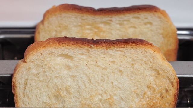 在粉红色的背景下，烤面包从白色的烤面包机里跳出来，特写视频下载