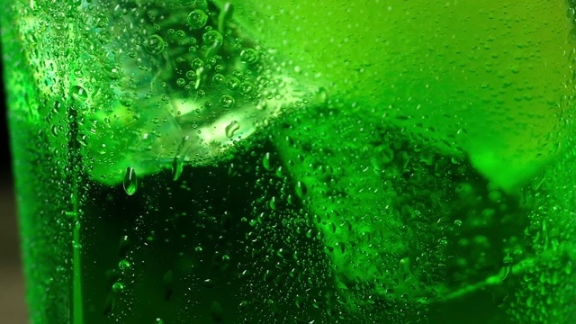 冰冷的冰块漂浮在绿色的泡沫鸡尾酒中旋转。视频下载