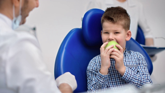 穿着制服的男牙医给快乐的孩子新鲜的绿苹果。红色摄像机中拍摄视频素材