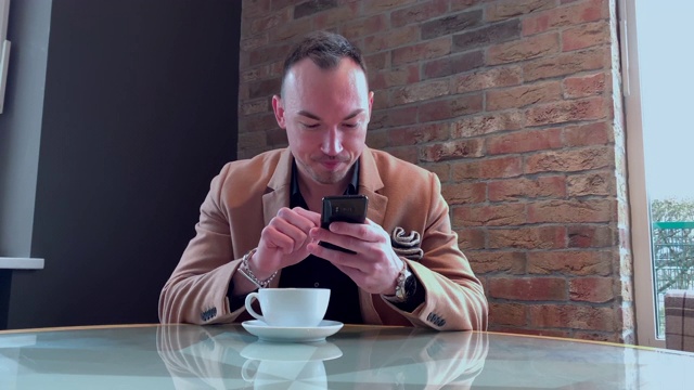 一个帅哥独自在咖啡馆喝大杯咖啡，在智能手机上写字视频素材