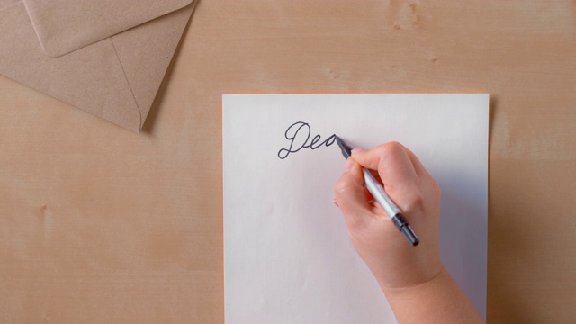 女性的手写着“亲爱的”在白色的纸的顶部视频素材
