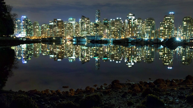 在加拿大温哥华的夜晚，在天空的映衬下，船停泊在海上，灯光建筑的反射视频素材