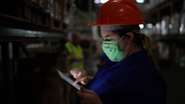 中年妇女的肖像戴着口罩使用数字平板电脑-工作在仓库/工业视频素材
