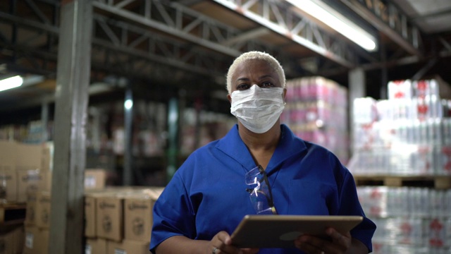 在仓库/工业中工作的妇女戴着面具使用数字平板电脑的肖像视频素材