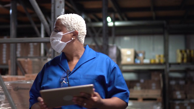 在仓库/工业工作的妇女戴着口罩用平板电脑走路视频下载