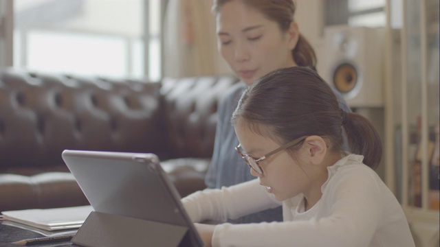 一个十几岁的女孩和她妈妈在家里用平板电脑学习视频下载
