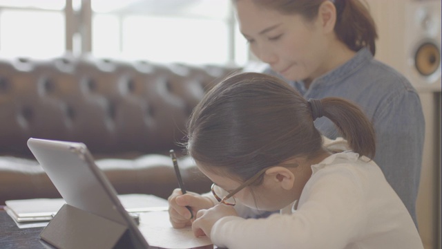 一个十几岁的女孩和她妈妈在家里用平板电脑学习视频下载