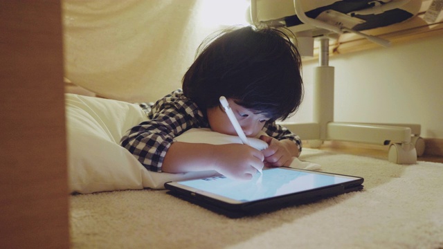 亚洲男孩做家庭作业与数字平板电脑躺在帐篷下从床视频素材