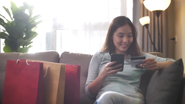 亚洲女人在家里用智能手机购物视频素材