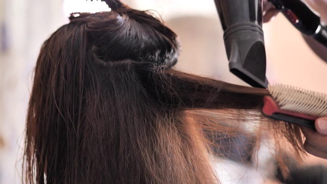 理发师用吹风机和圆刷吹干顾客的头发。视频下载