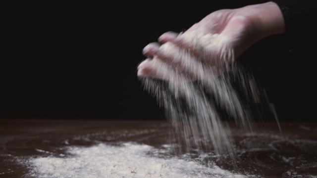 面粉从手中滑落。制作的特写和准备面粉的家庭烘焙。女人的手在撒面粉。厨师将面粉撒在黑色背景的木桌上视频素材