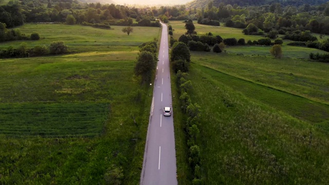 在金色的夏日落日下，一辆灰色的汽车行驶在空旷的乡村道路上视频素材