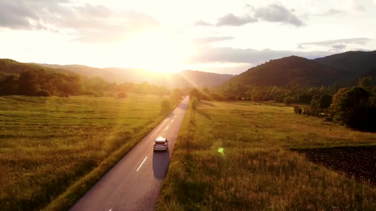 在金色的夏日落日下，一辆灰色的汽车行驶在空旷的乡村道路上视频下载