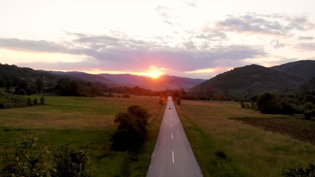 在金色的夏日落日下，一辆灰色的汽车行驶在空旷的乡村道路上视频素材