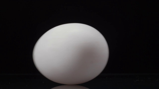 白色的鸡蛋在黑色的背景上旋转，有着美丽的倒影。近距离播放4K视频视频下载