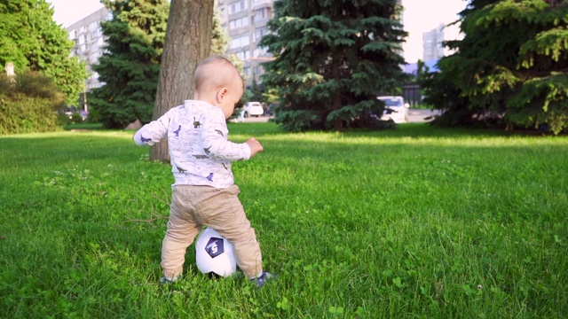 一岁的婴儿在公园里跑步和踢足球。慢动作视频下载