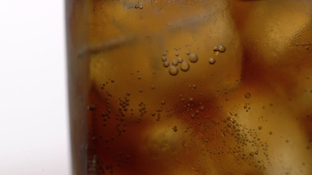 近距离拍摄的泡沫上升在可乐杯与冰。大量的含咖啡因的碳酸冰饮料视频下载