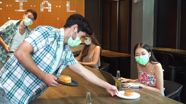 在假日期间，戴口罩的亚洲朋友在酒店餐厅或自助餐厅享用午餐，并保持社交距离，以保护新冠肺炎疫情。多民族观念中的新常态和面罩及面罩。视频下载