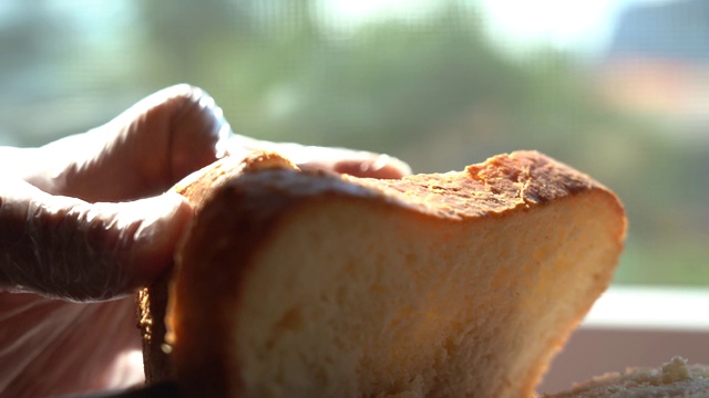 切一片面包。新鲜的面包放在靠近窗户的桌子上，被早晨的阳光照亮。健康饮食和传统烘焙的概念视频下载