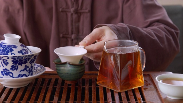 茶师将刚泡好的茶从盖碗中倒入筛子至玻璃杯壶中。男子将热茶饮料倒进玻璃杯、茶壶和托盘上，同时进行传统仪式。视频素材