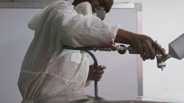 非裔美国男性汽车修理工穿着西装用喷枪给一辆车的零件喷漆视频下载