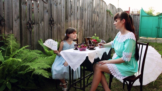 一个小女孩和她的妈妈坐在院子里的桌旁。视频素材