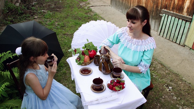 一个穿着漂亮裙子的女孩正在和她的妈妈喝茶。视频素材