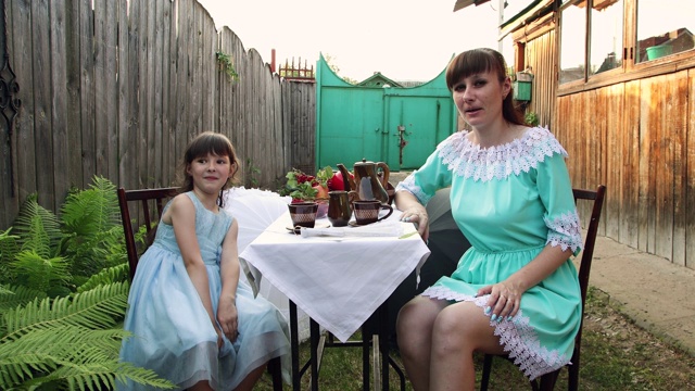 一个女孩和她的母亲坐在院子里同一张桌子微笑着。视频素材