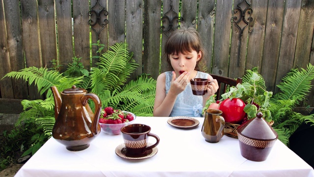 一个小女孩喝茶，吃浆果，舔手指。视频下载